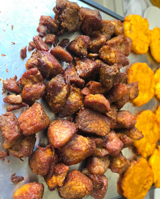 Haitian griot fried pork pieces beside golden fried plantains on a preparation surface